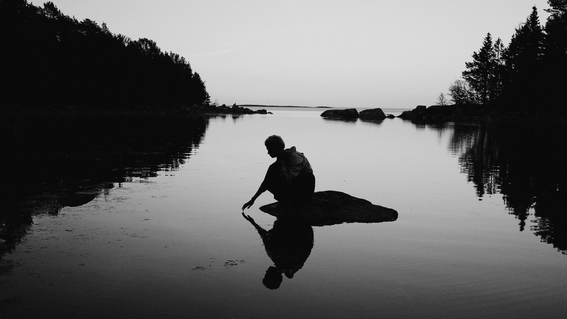 Solitary figure crouching on a rock in still water at dusk