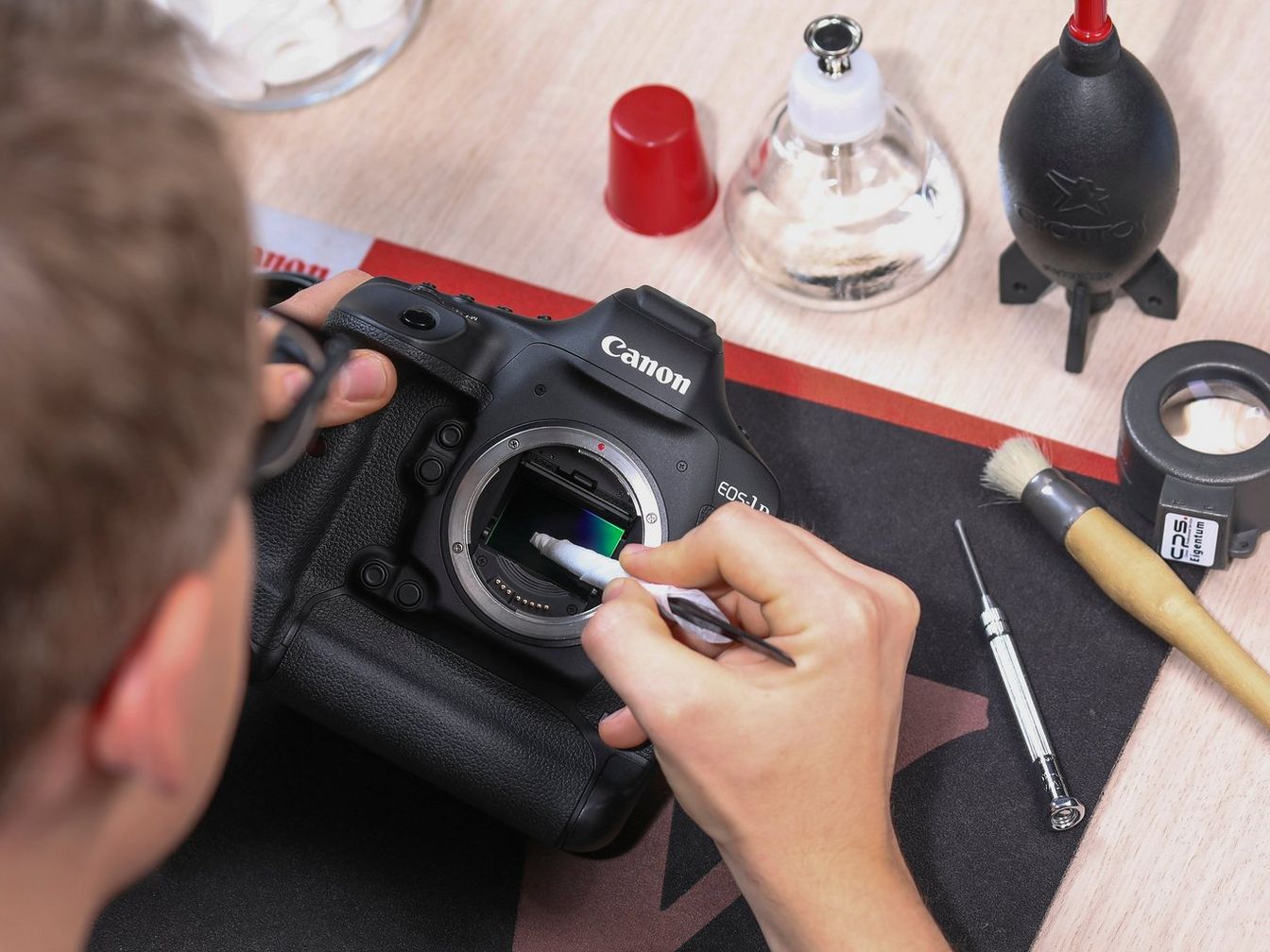 A Canon body with the mirror up, sensor being cleaned with a swab